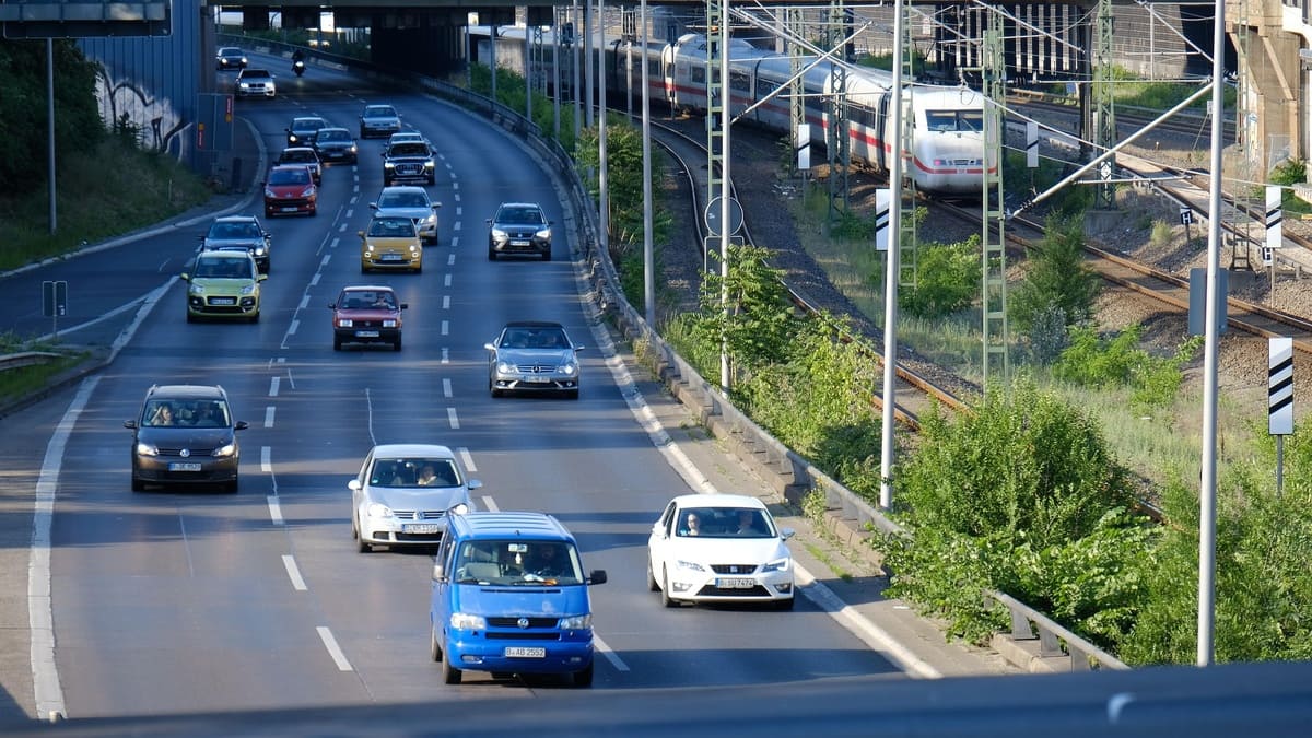 線路の脇を車が走り、列車が通り過ぎる。道路と線路には緑が並んでいる。